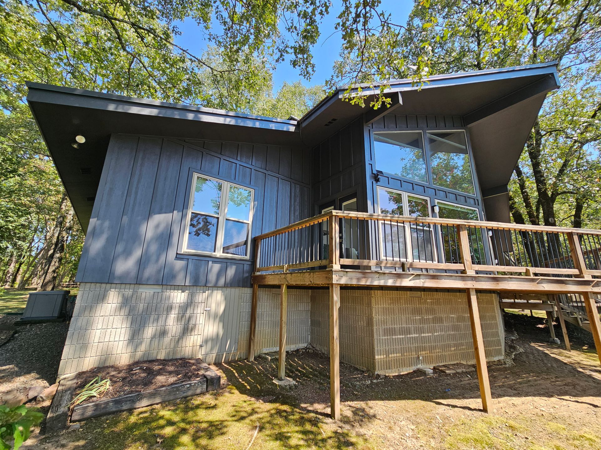 A small house with a large deck in the middle of a forest.