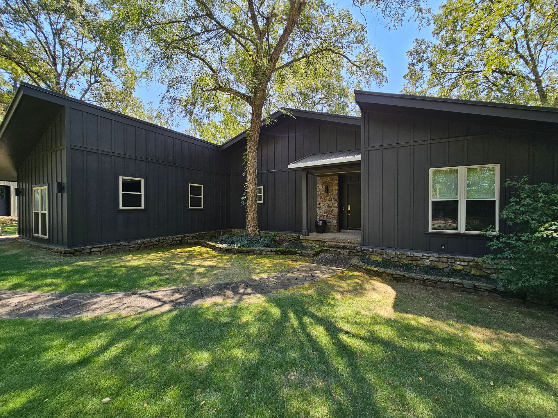 A large black house with a lot of windows and a tree in front of it.