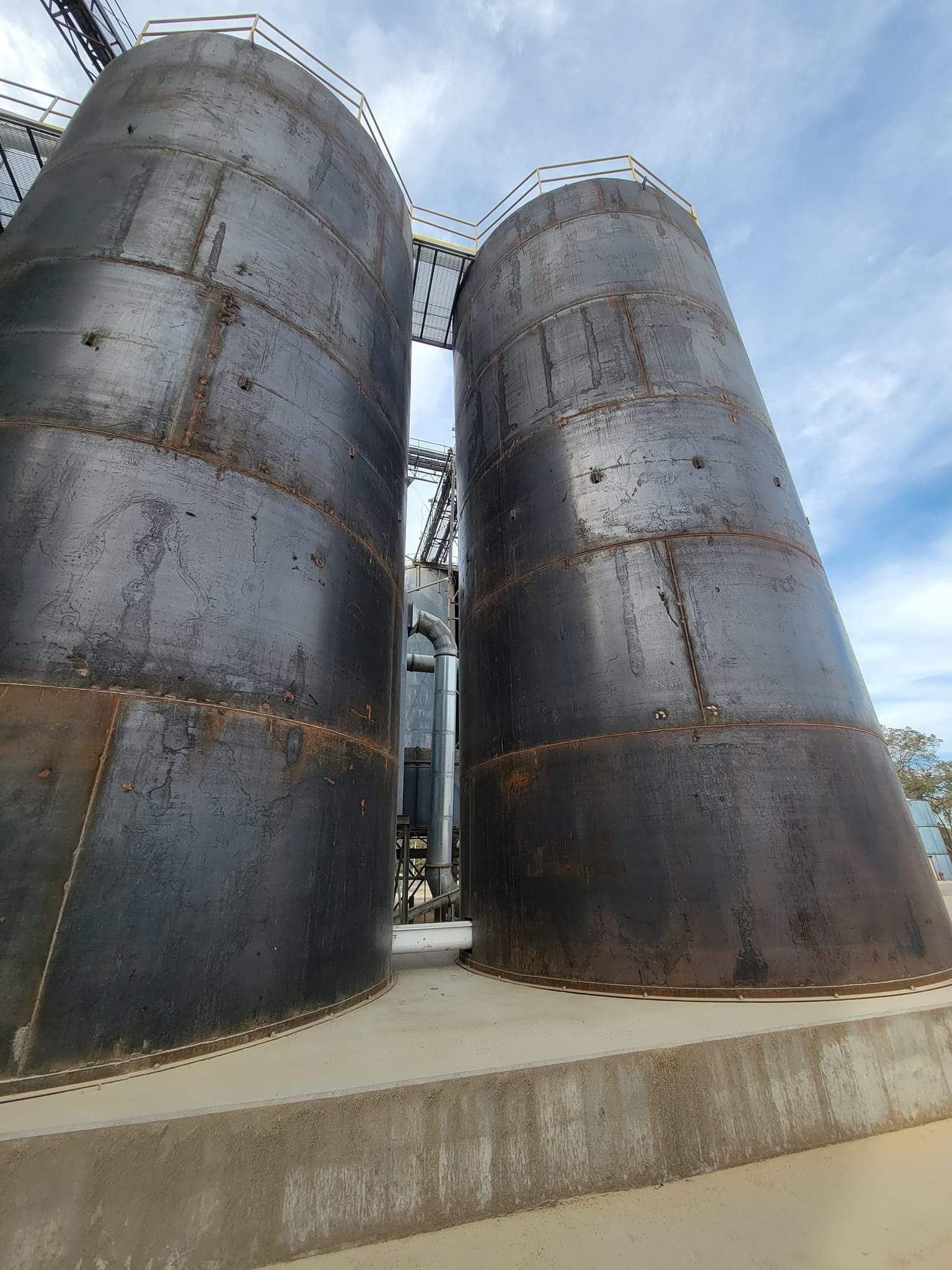 Two large metal silos are sitting next to each other on a concrete platform.
