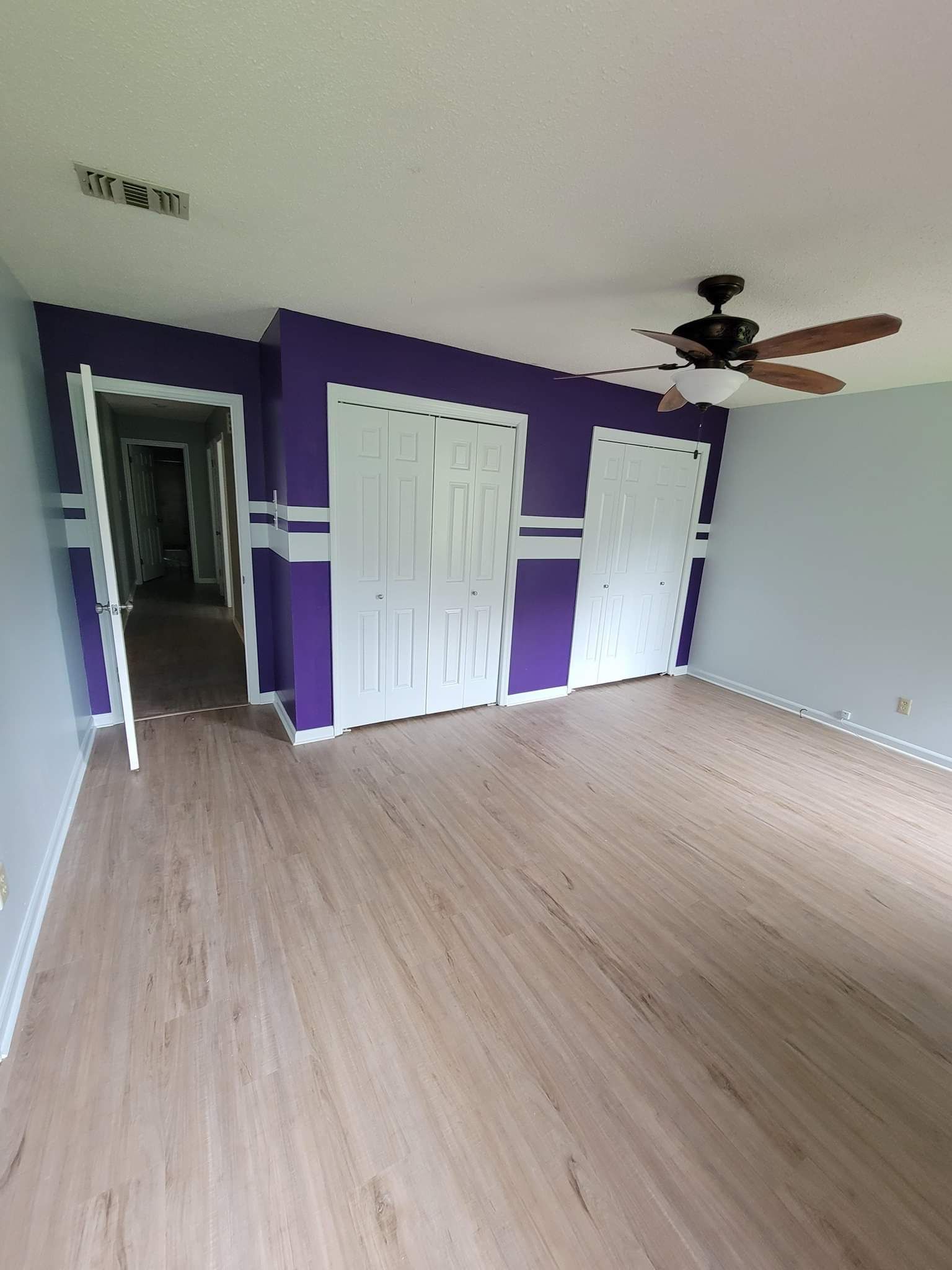 An empty room with purple walls and a ceiling fan.