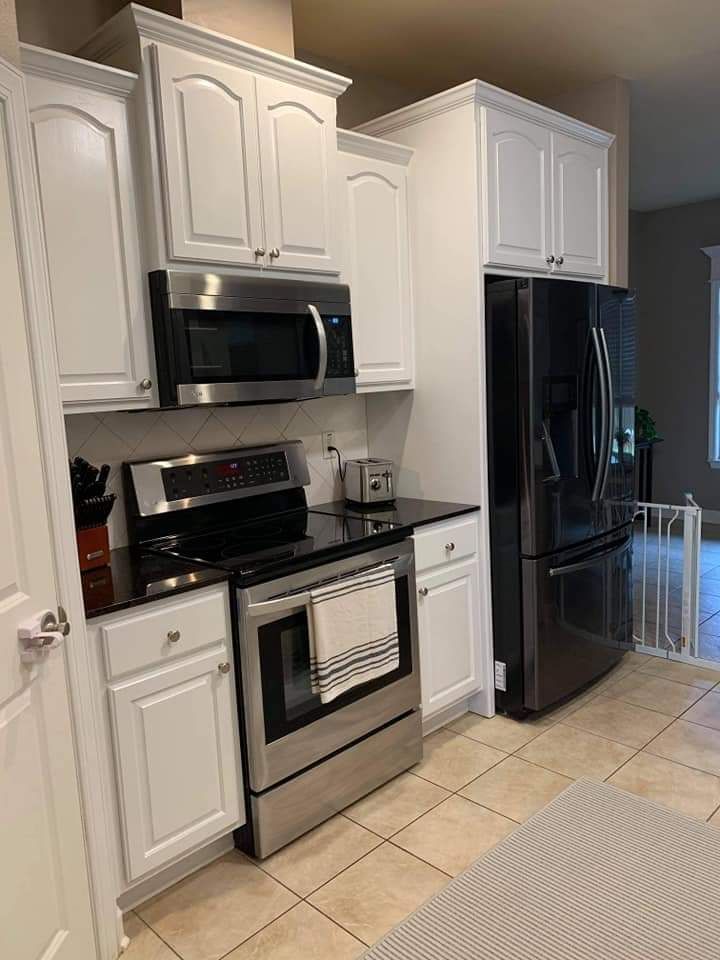 A kitchen with white cabinets , stainless steel appliances , and a black refrigerator.