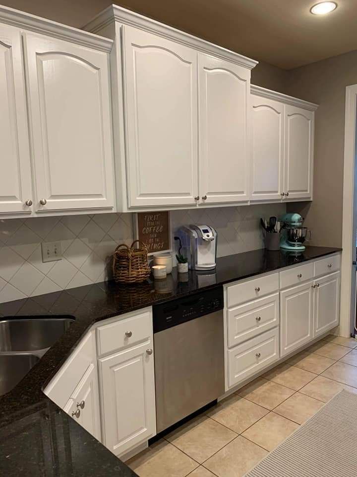 A kitchen with white cabinets , black counter tops , a stainless steel dishwasher , and a sink.