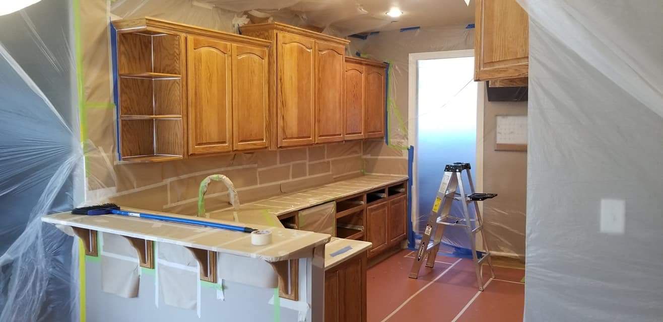 A kitchen with wooden cabinets and a ladder is being painted.