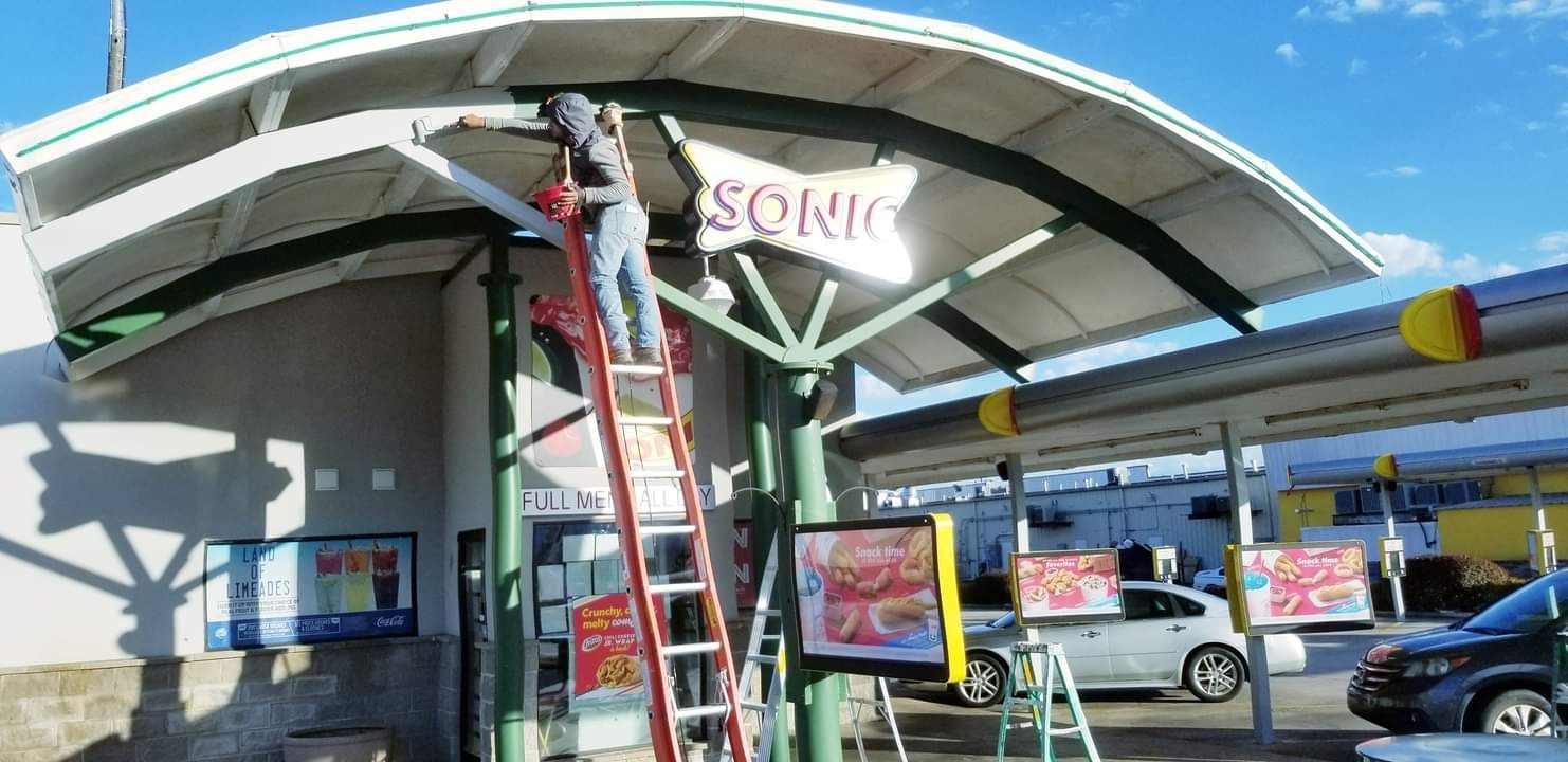 A man is standing on a ladder in front of a sonic restaurant.