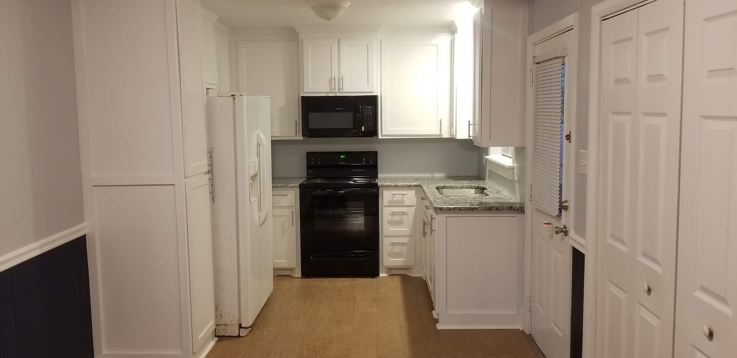 A kitchen with white cabinets , a black stove , a refrigerator , and a microwave.