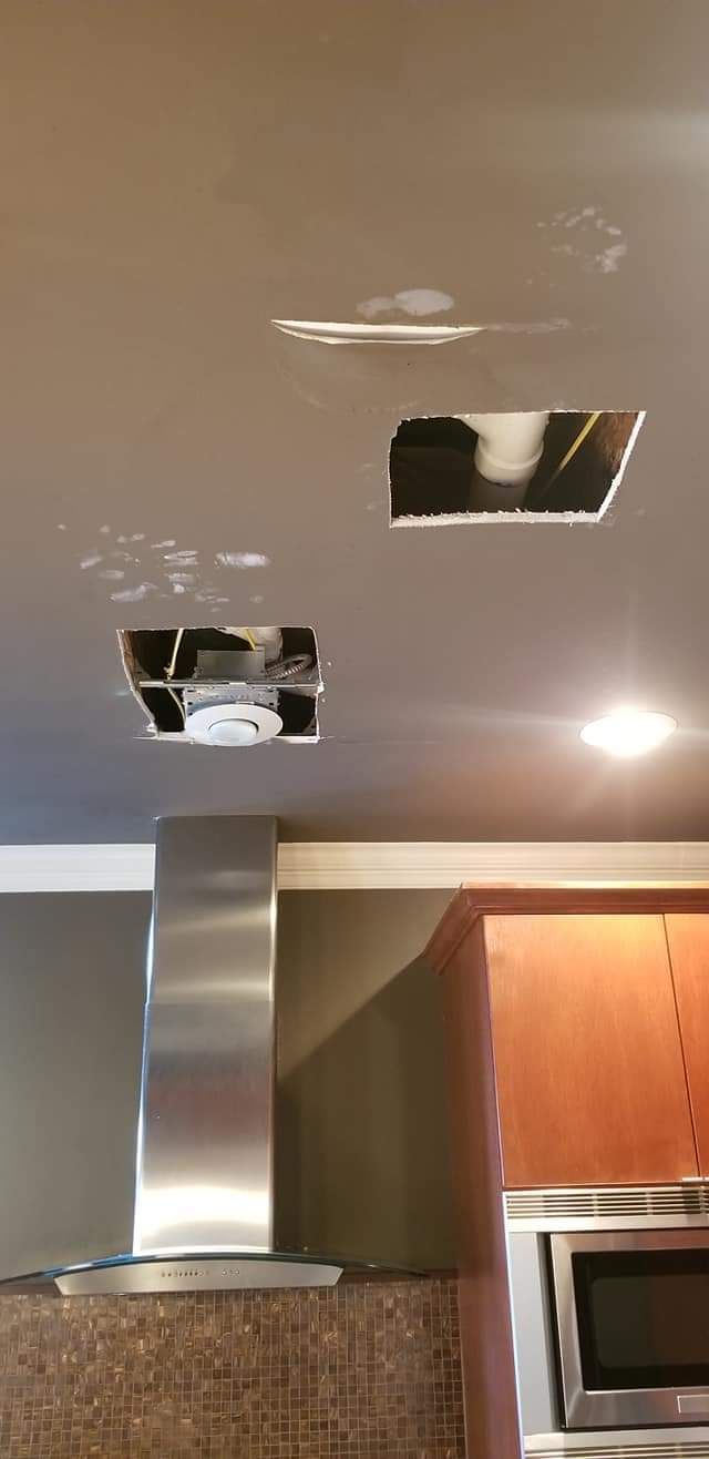 A kitchen with a stainless steel hood and two holes in the ceiling.