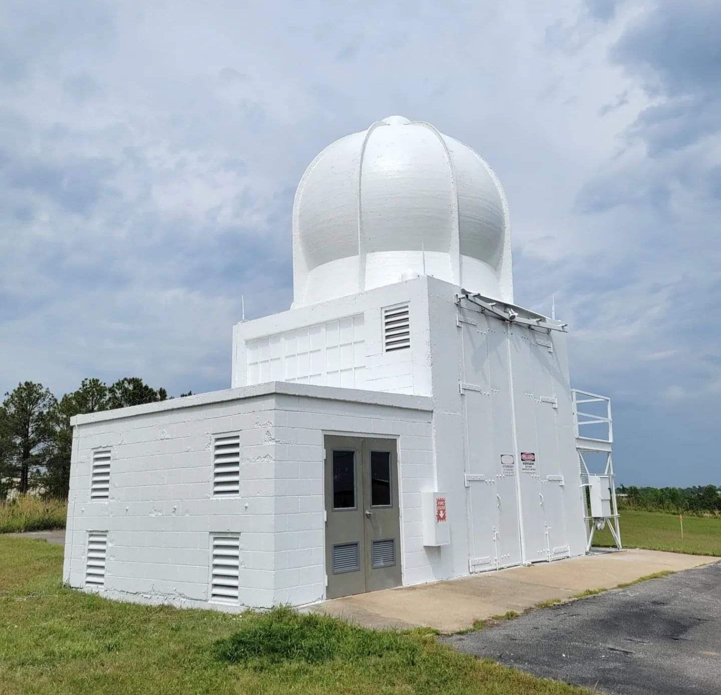 A white building with a dome on top of it is sitting in the middle of a field.