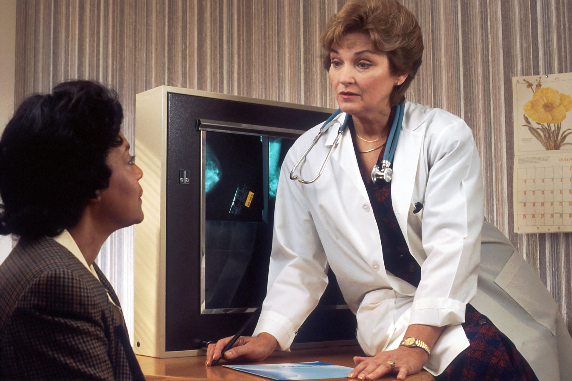 Doctor in white coat consulting with patient at a desk, examining medical scans.