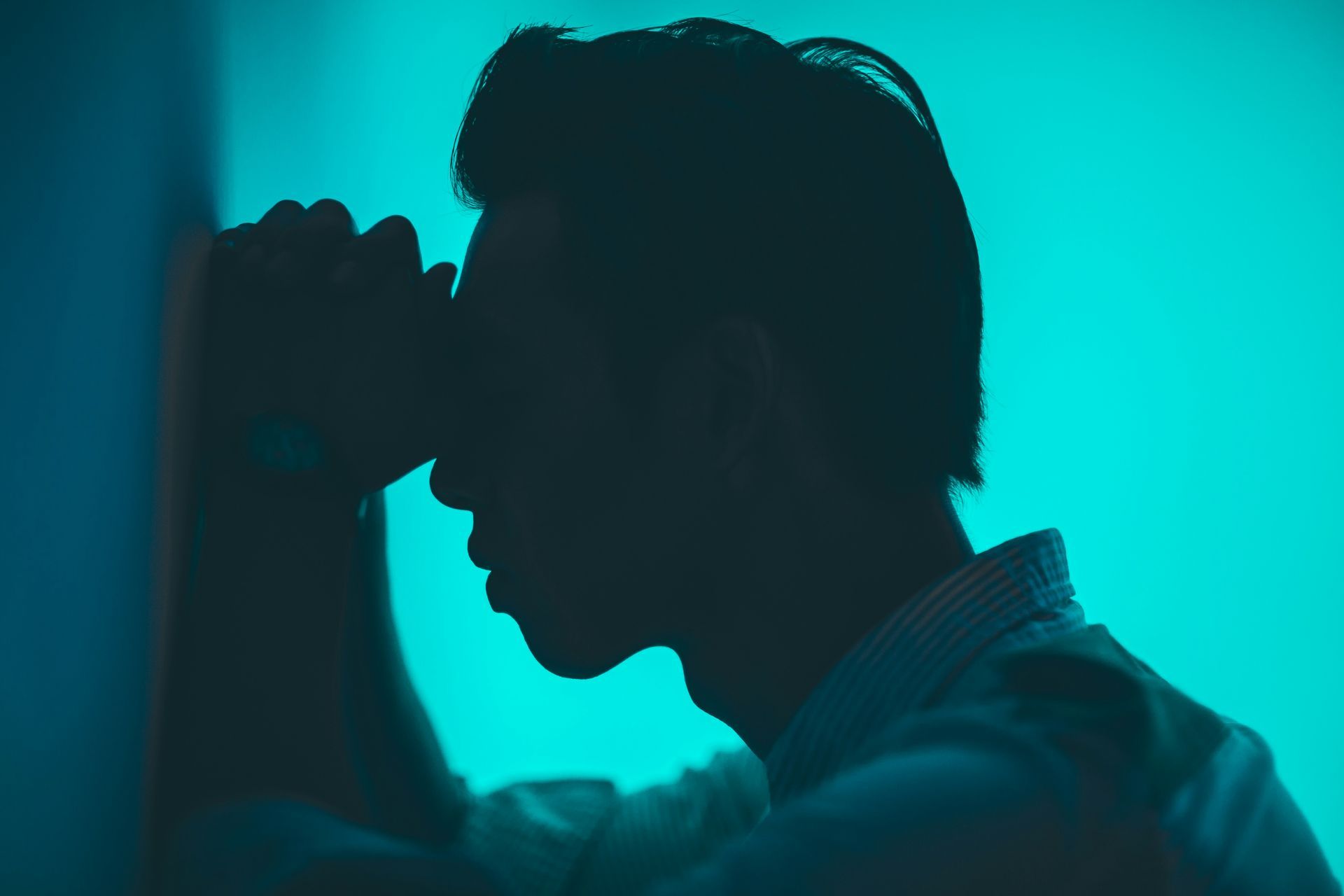 Silhouette of a person with head in hands against a teal background, appearing stressed.