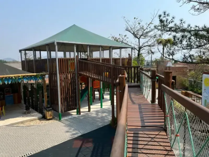Estrutura de parque infantil com ponte de madeira, telhado verde e diversas atrações lúdicas.