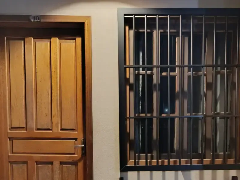 Porta e janela de madeira com grades de segurança pretas em parede bege.