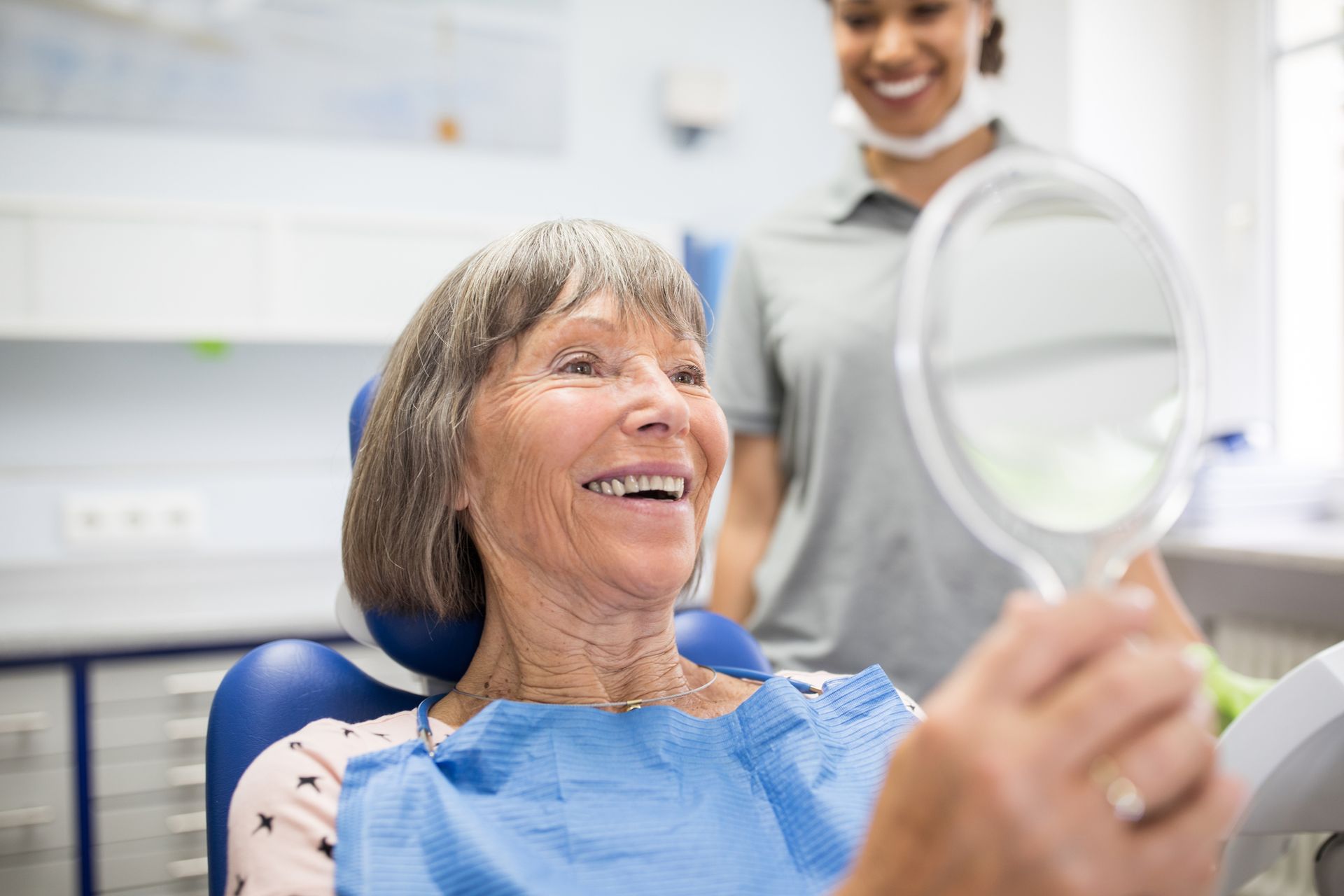 An elderly woman looking into a mirror after a dental treatment.