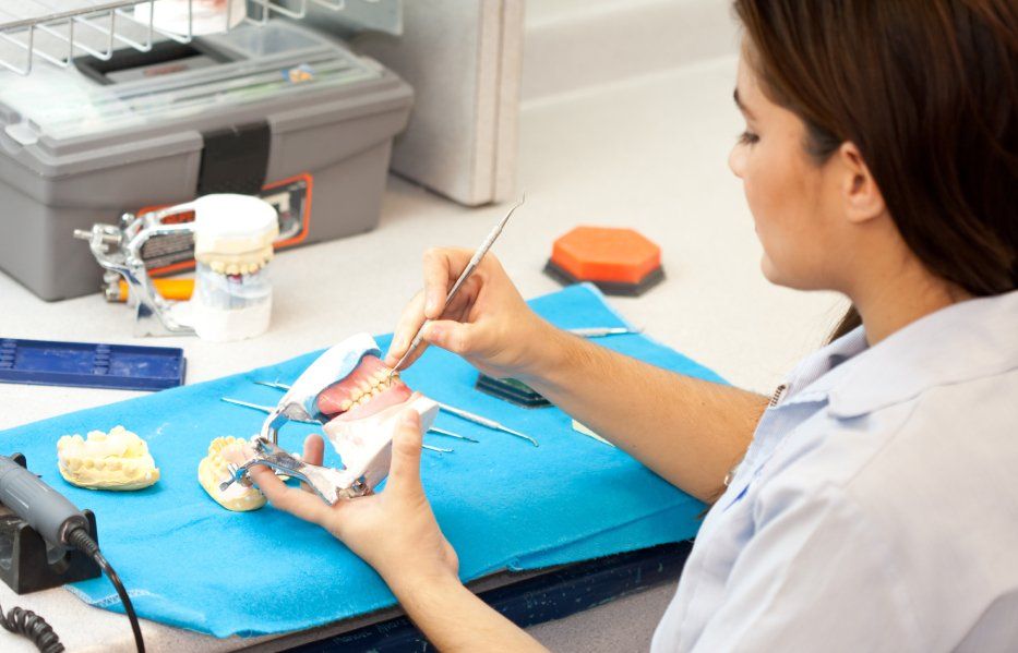 Dentist working on dentures in a dental lab, using tools, on a blue surface.