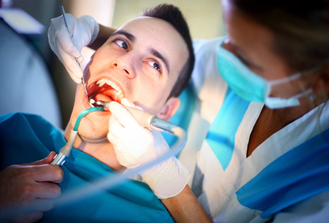 Person receiving dental work; dentist and tools in mouth.
