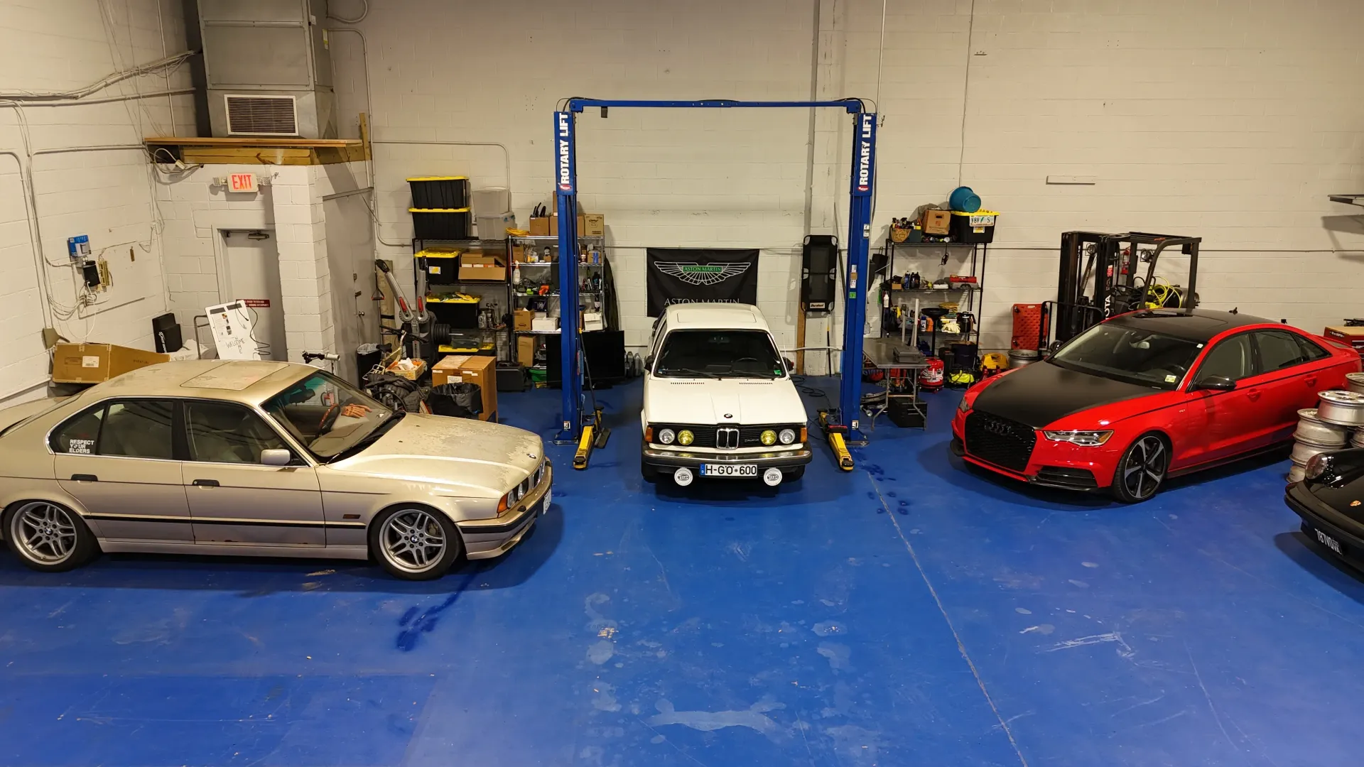Cars in a garage, including a gold sedan on the left, a white car in the center, and a red car on the right.