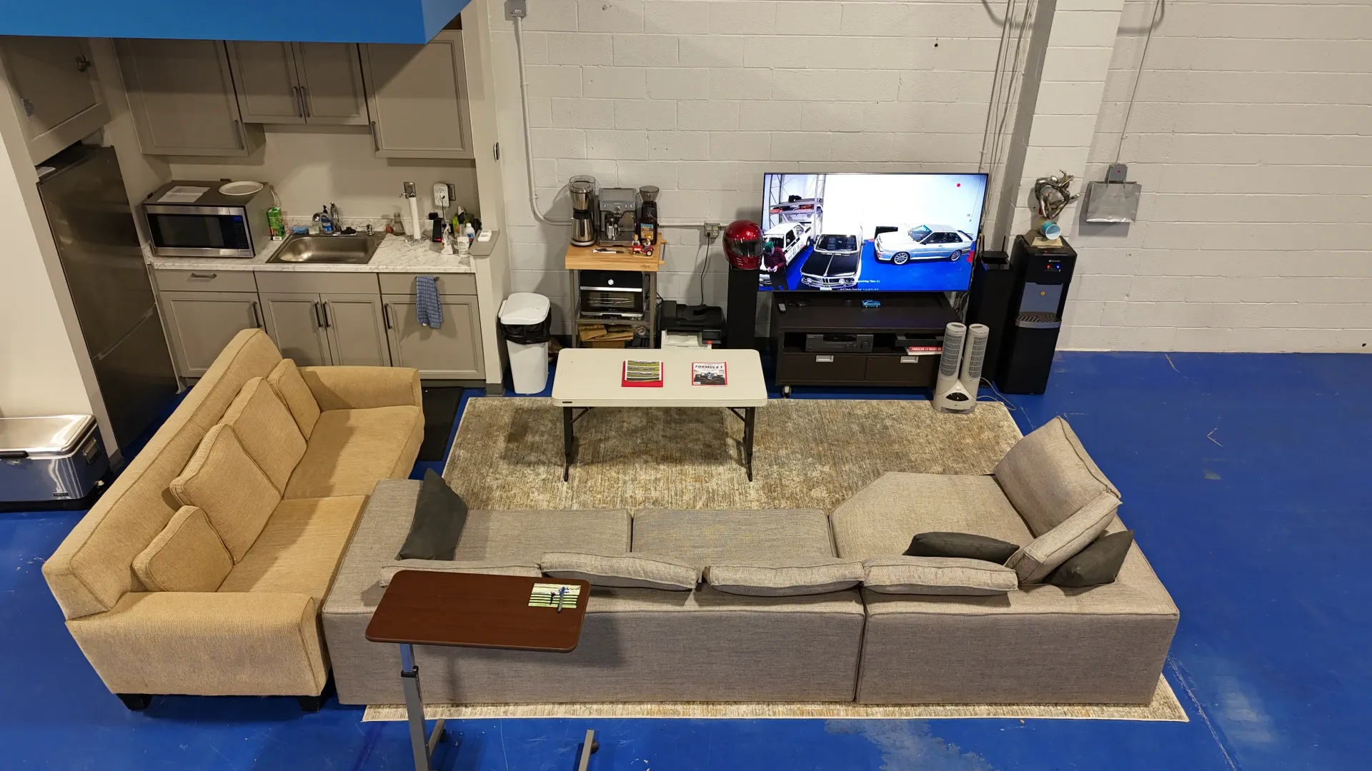 Living room area with a sectional sofa, TV, small kitchen, and a blue floor.