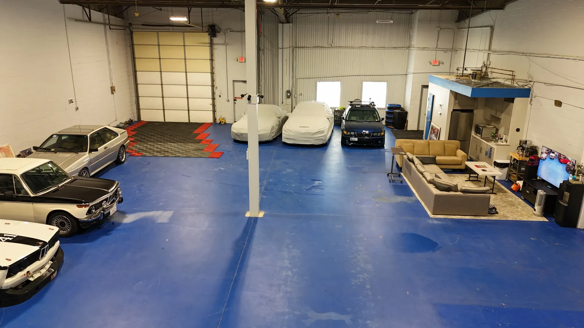 Large garage with multiple cars, some covered, blue floor, and a seating area.