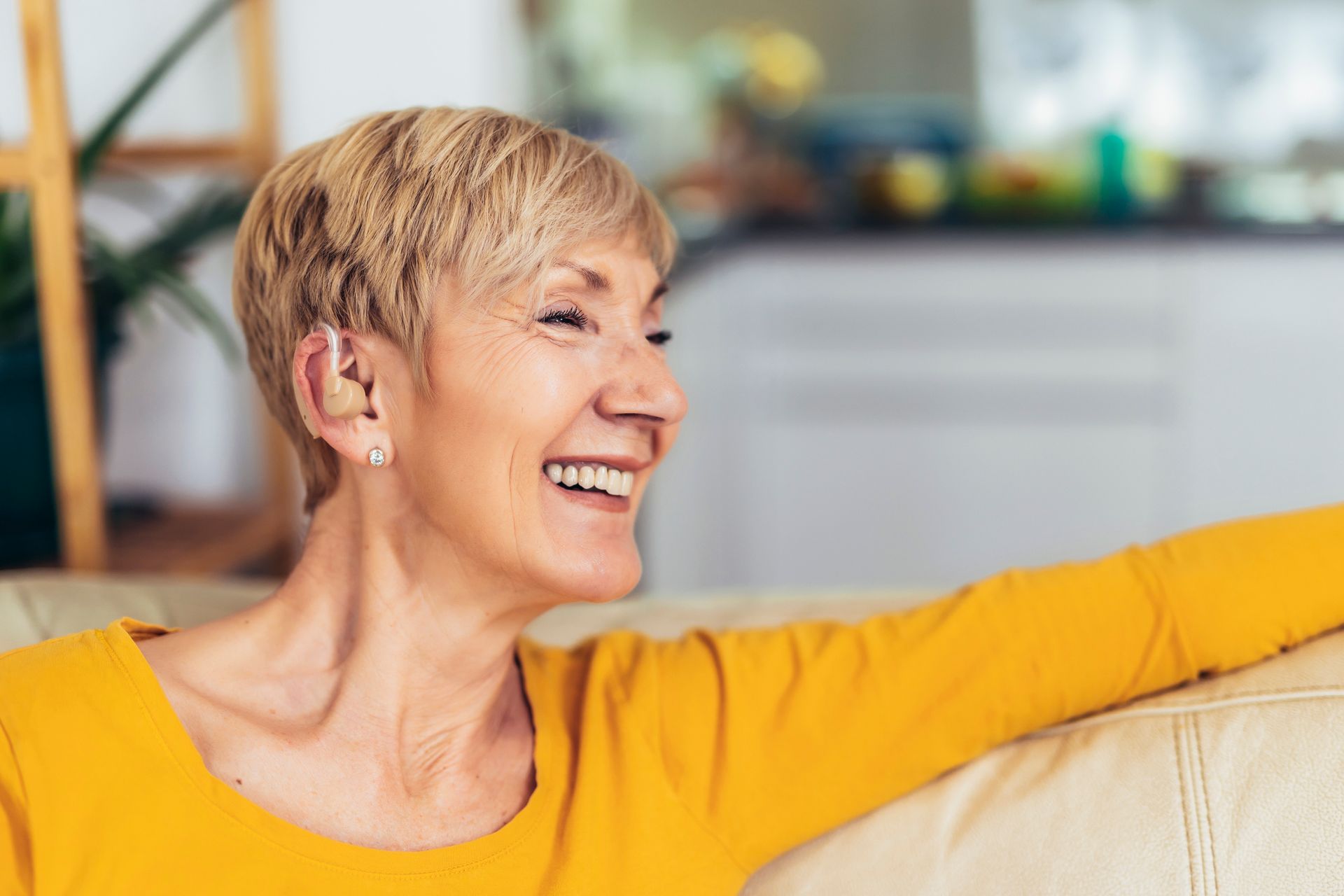 A woman in a yellow sweater is sitting on a couch and smiling.
