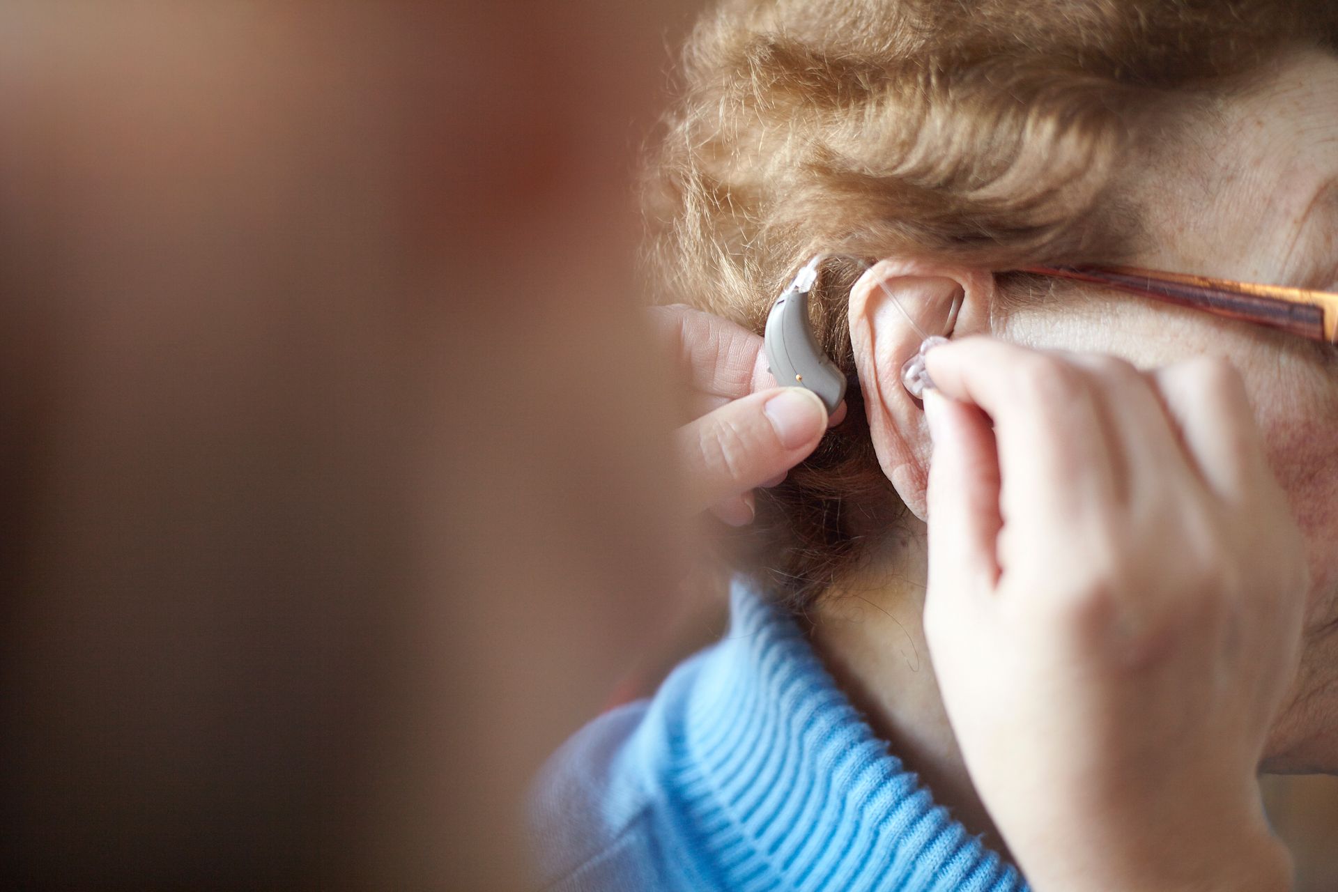 A woman is putting a hearing aid in her ear.