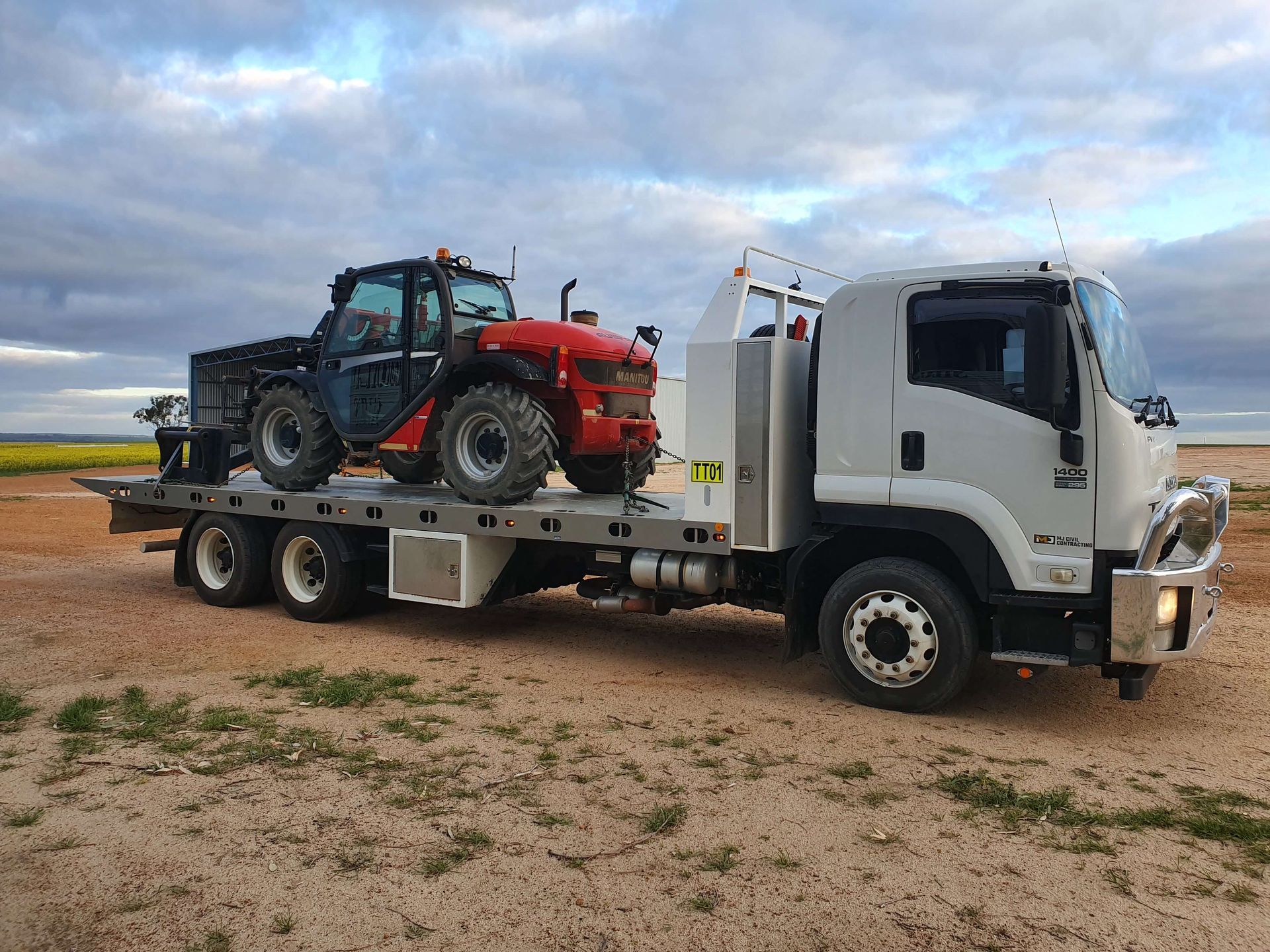 A tow truck is carrying a tractor on the back of it.