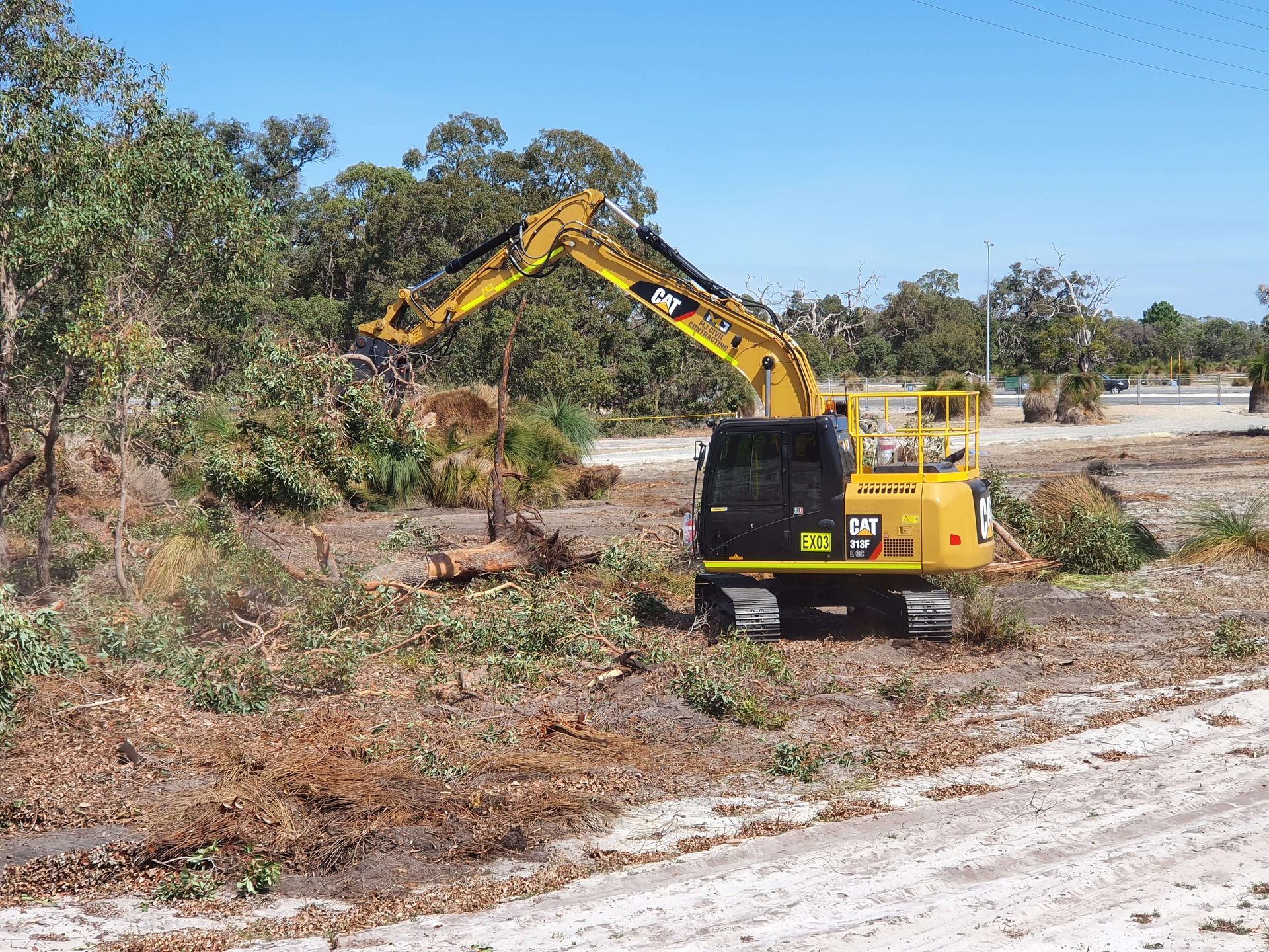 A yellow excavator is working in a field with trees in the background.