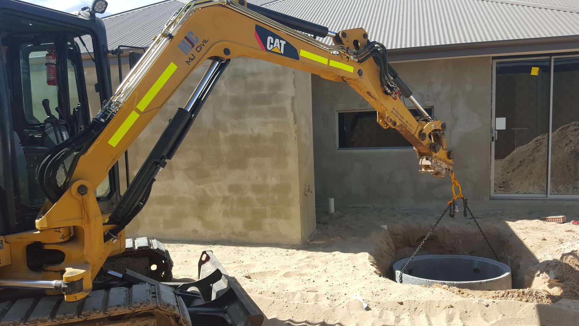 A cat excavator is lifting a concrete ring into a hole.