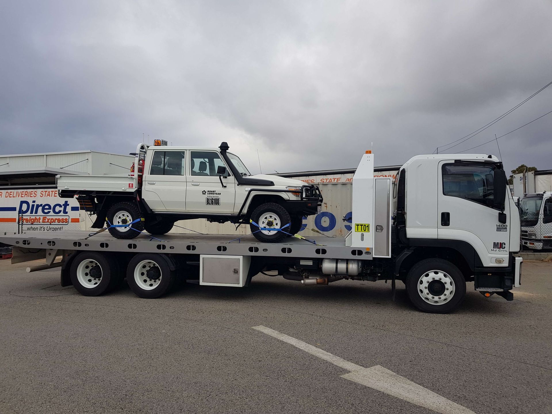 A white tow truck is carrying a white truck on the back of it.