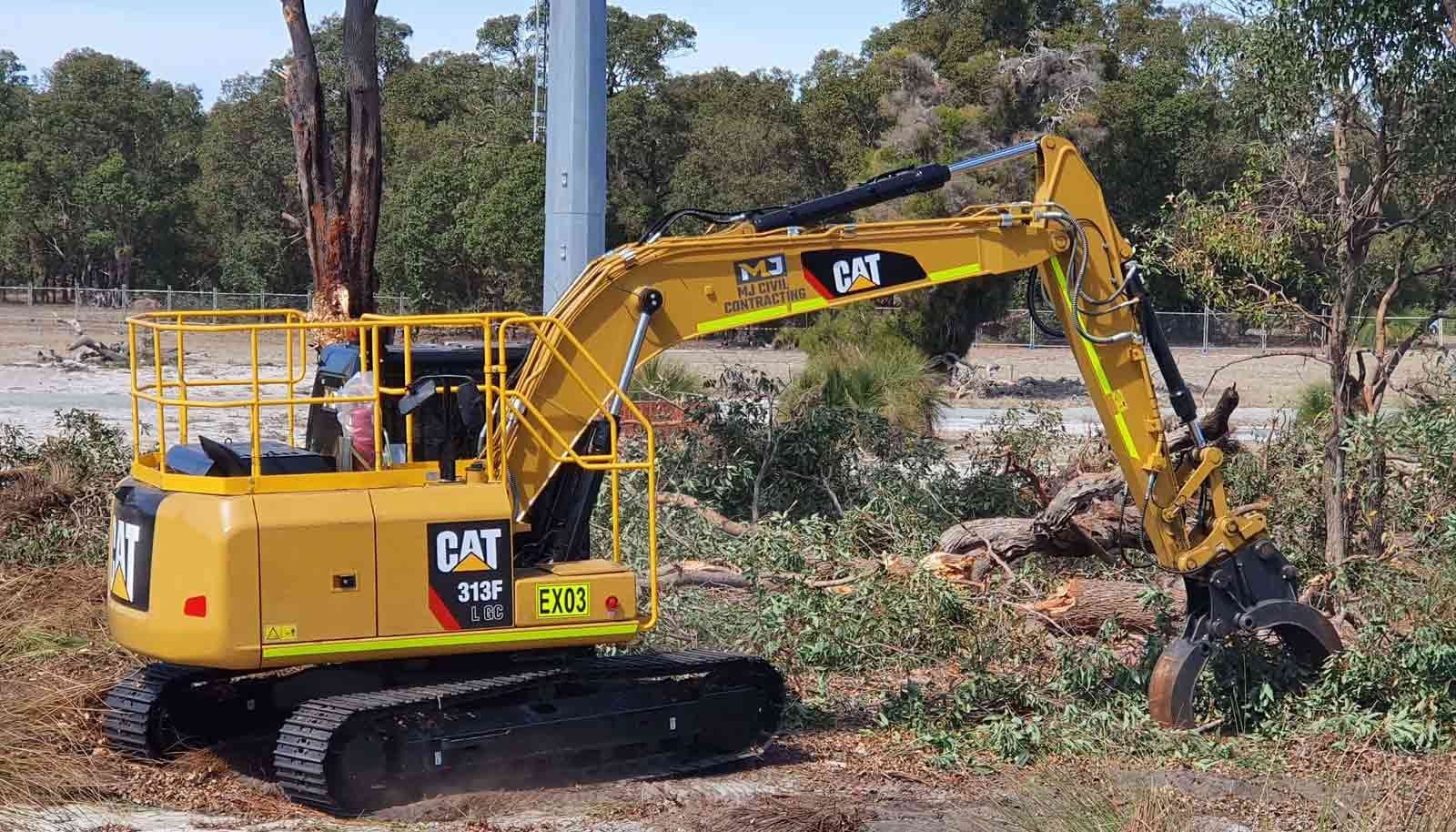 A yellow cat excavator is cutting down trees in a field.