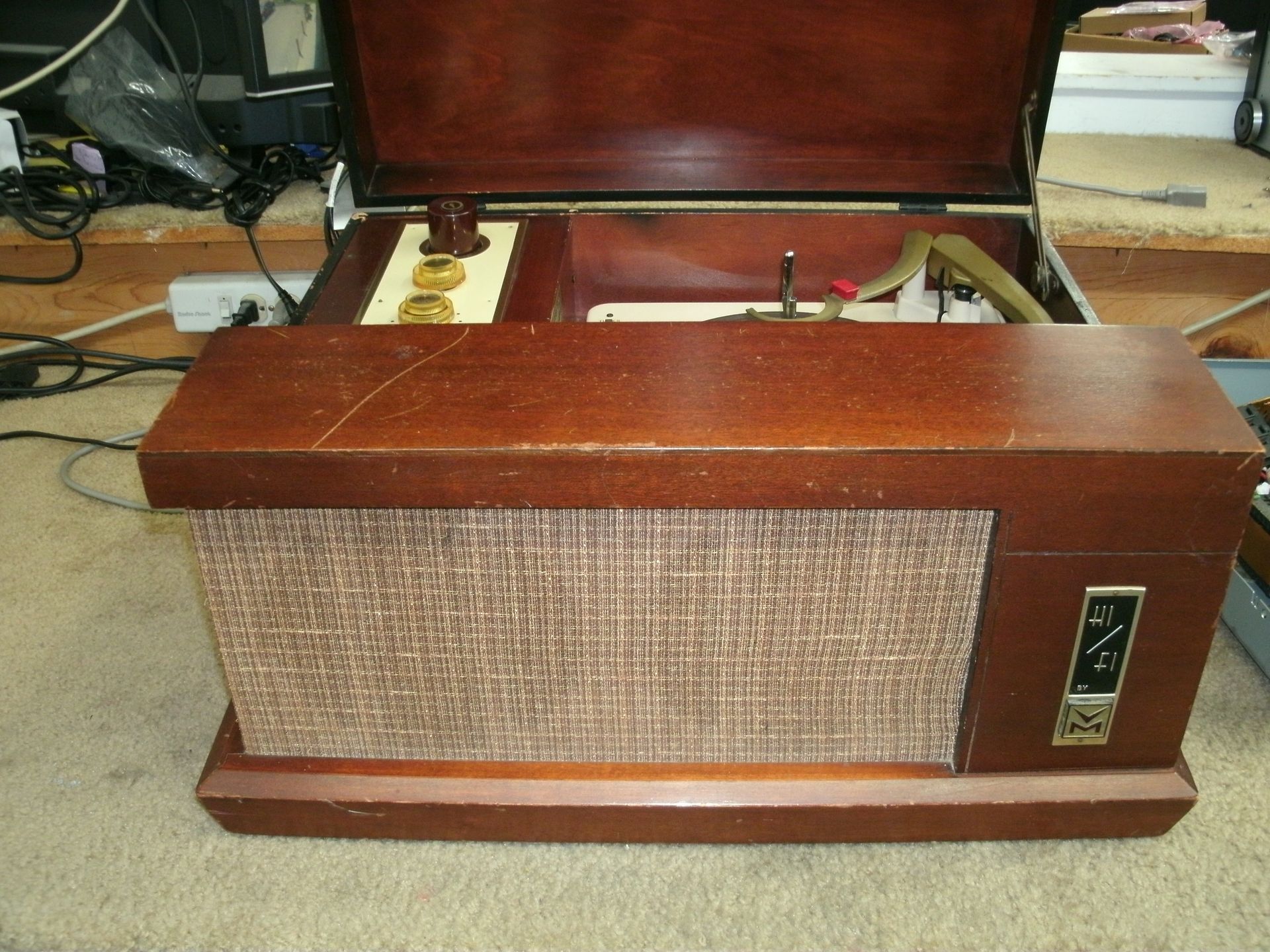 Vintage wooden radio with open lid and fabric speaker grille on a carpeted floor