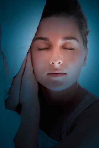 Donna con gli occhi chiusi, le mani vicino al viso, bagliore arancione sul viso su sfondo blu.