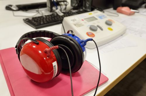 Cuffie insonorizzate rosse e blu su una cartella rosa accanto a un audiometro su una scrivania bianca.