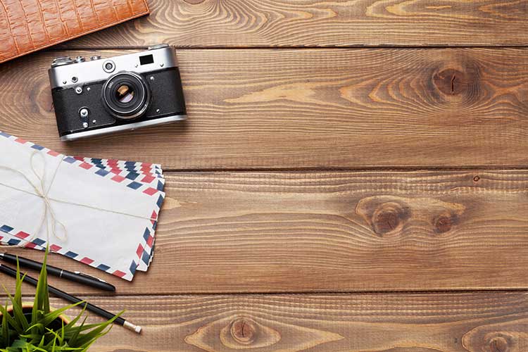 A wooden table with a camera , envelopes , a pen and a wallet.