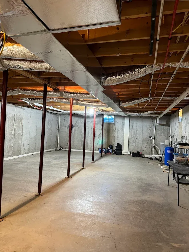 Bare concrete basement with support beams, ducts, and pipes.