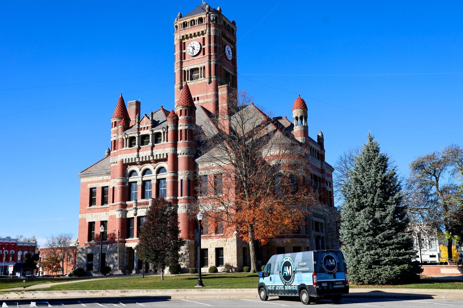 Clock tower on brick building; parked van in foreground.
