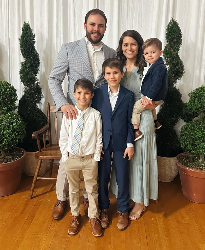 Family of five in formal attire posing in front of decorative topiaries.