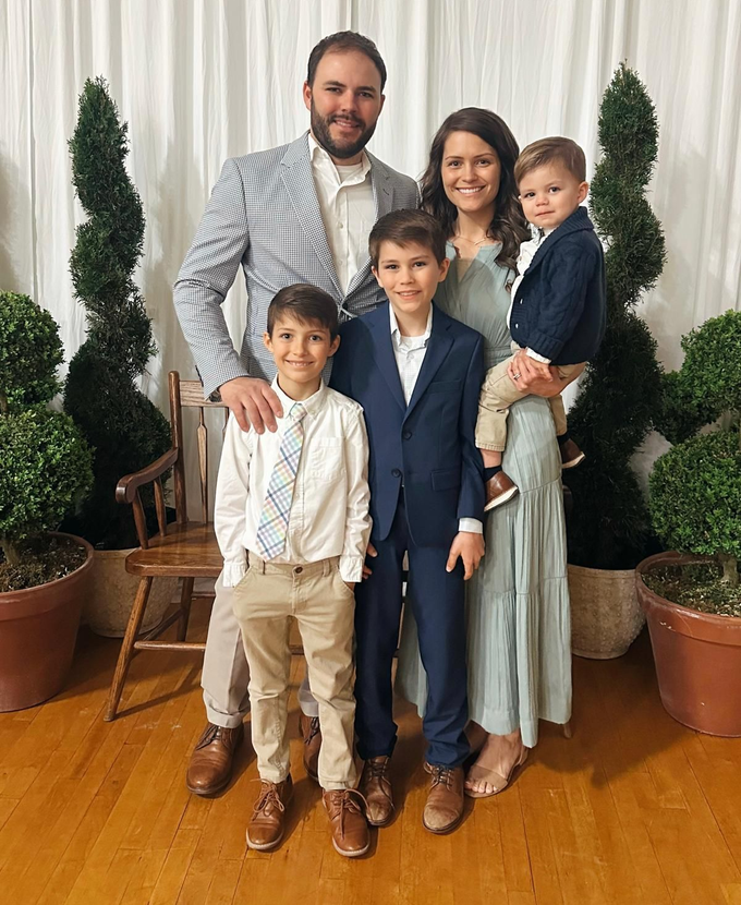 Family posing indoors, in front of a white backdrop, with two topiary trees.