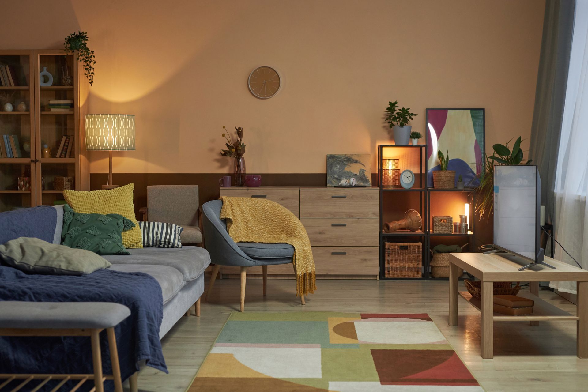 Cozy living room with sofa, chair, and TV, warm lighting, wooden furniture, and colorful rug.