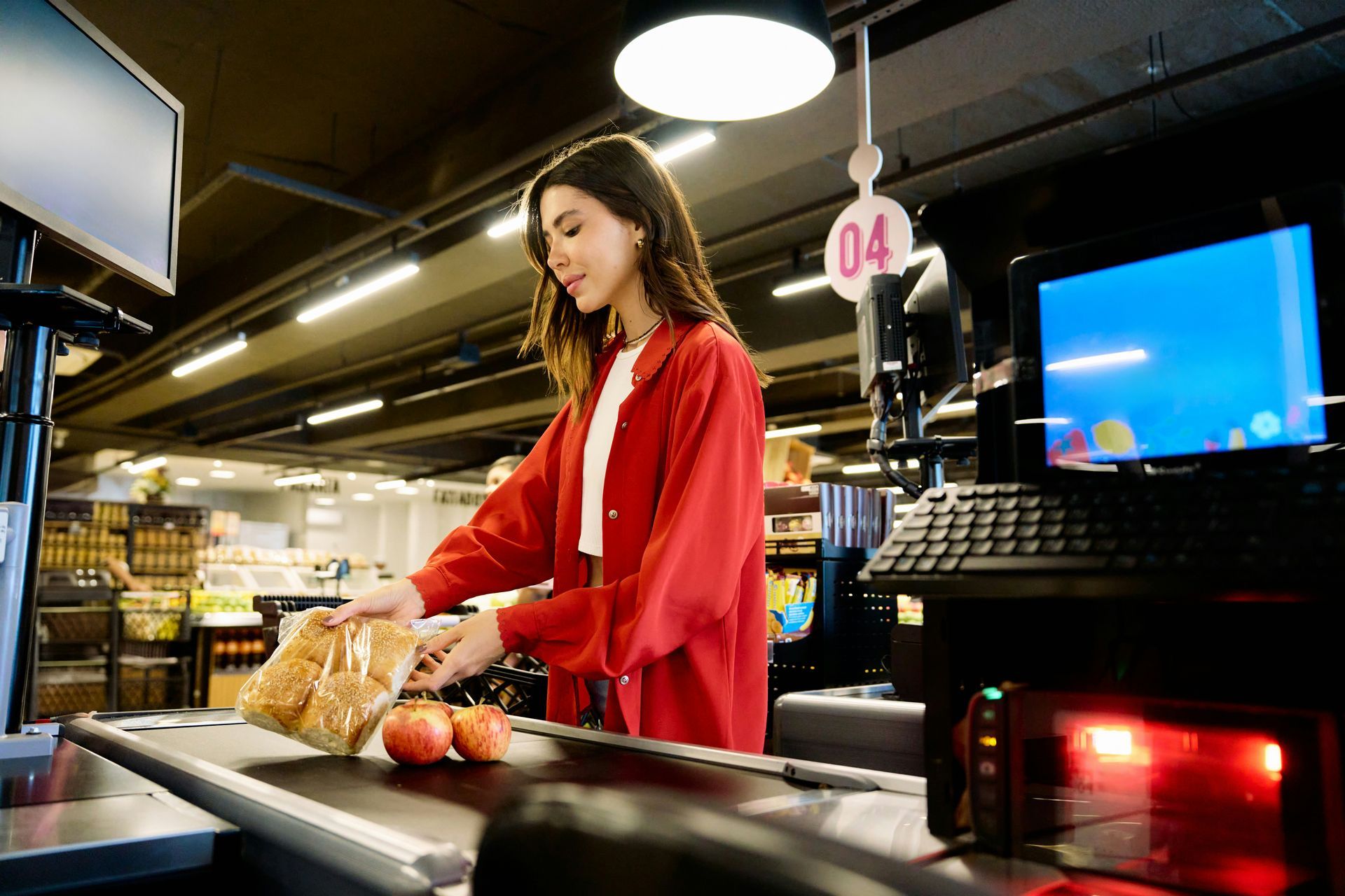 Woman in red shirt places groceries on a supermarket checkout conveyor belt.