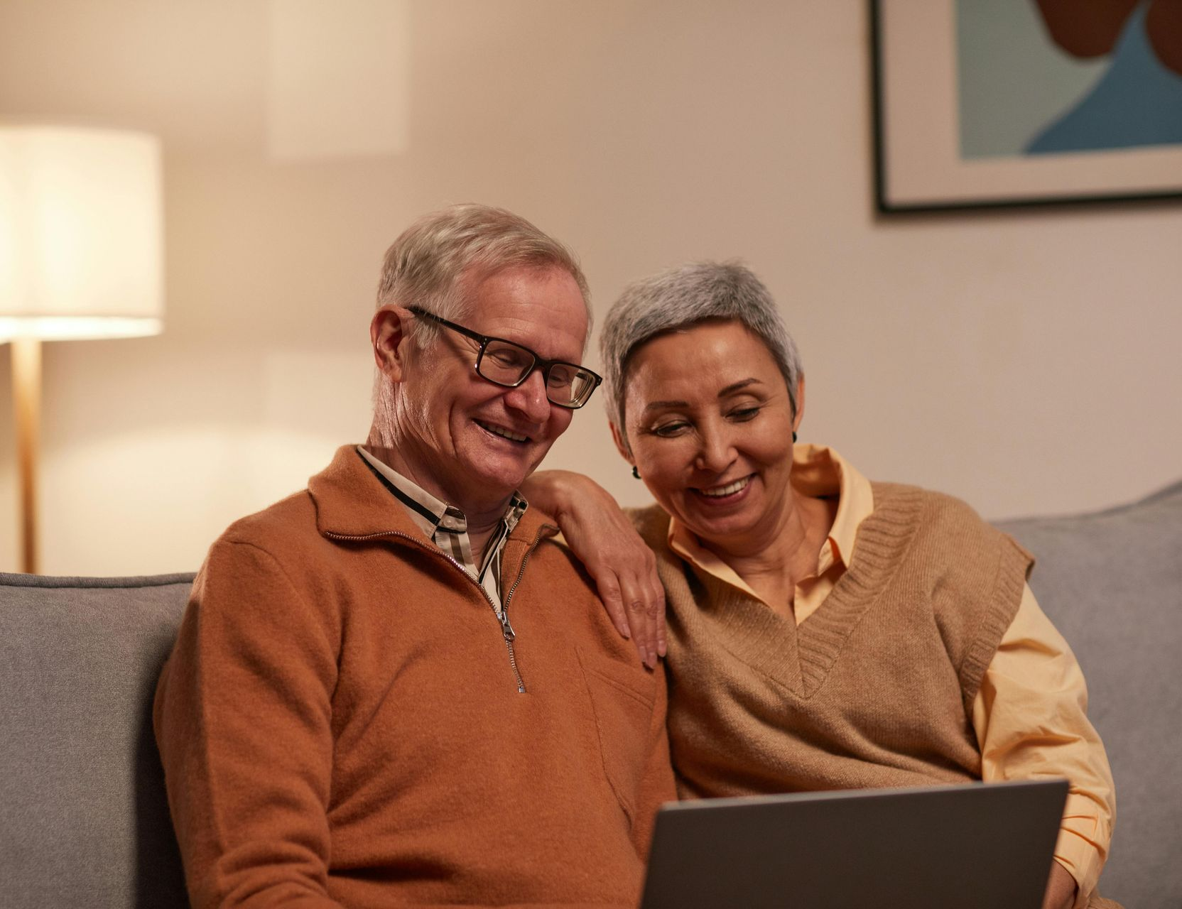 Couple smiles while looking at a laptop together on a couch.