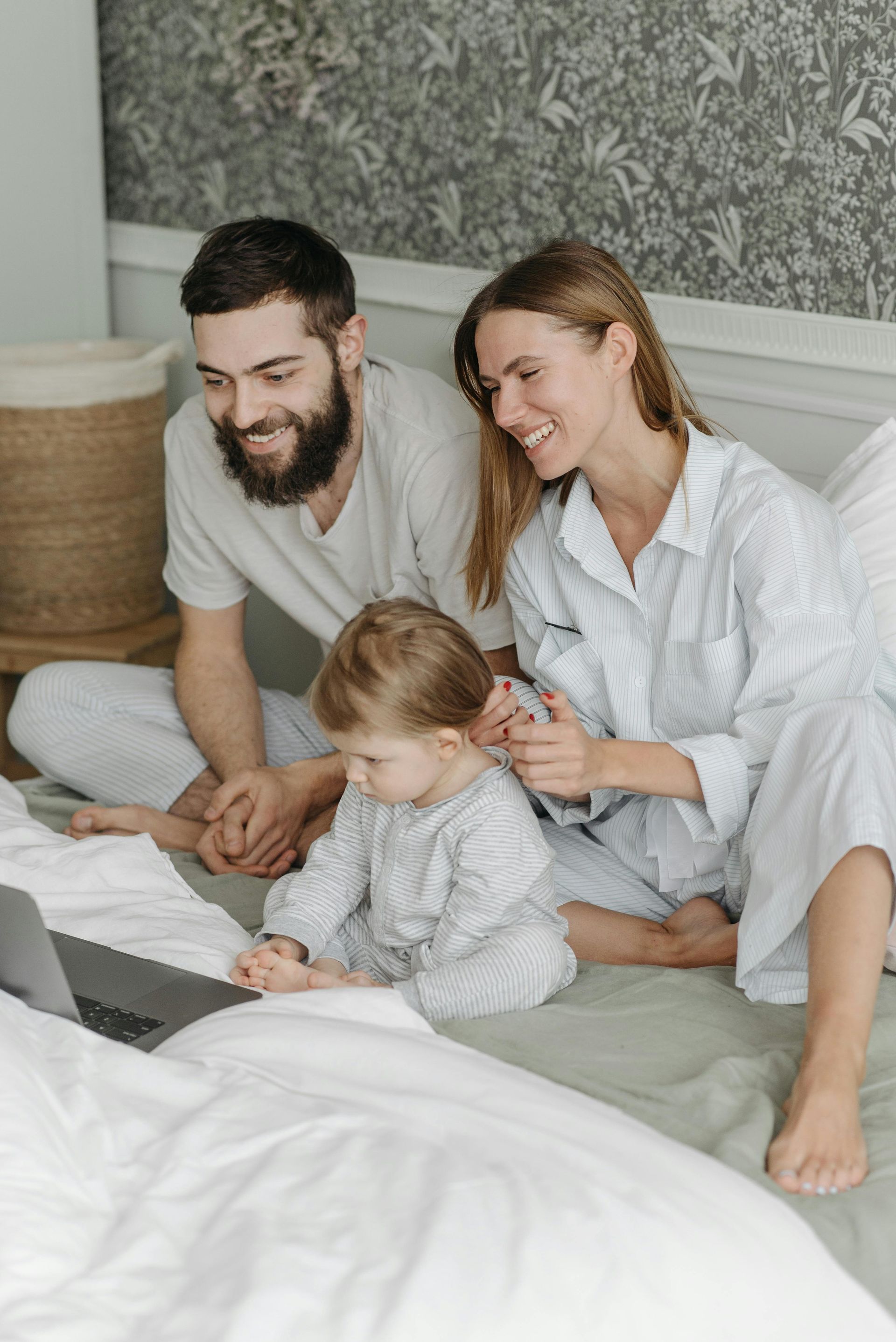Family in pajamas on bed looking at laptop, smiling.