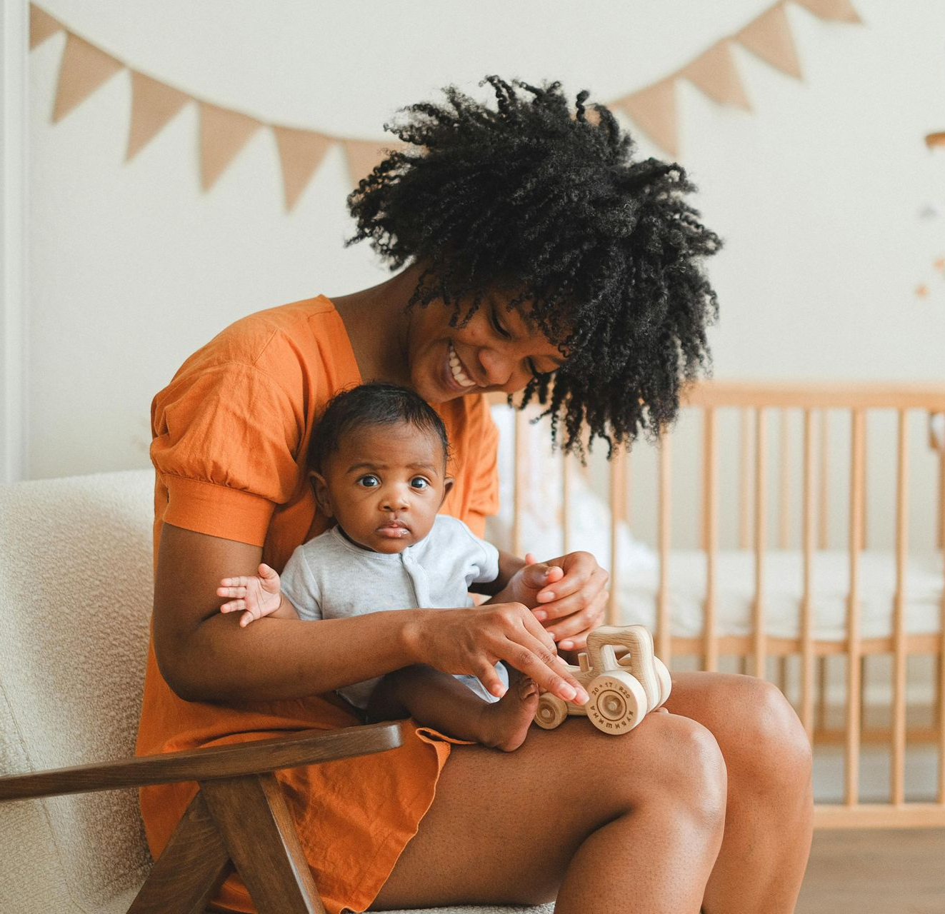 Woman seated holding a baby, smiling. They are in a nursery.