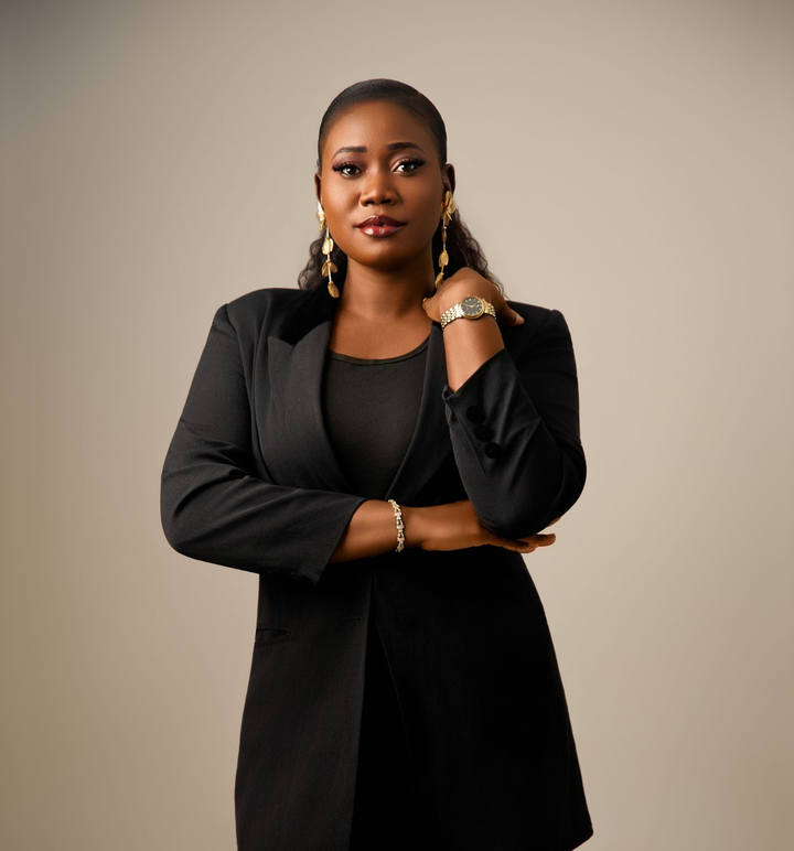 Studio portrait of a woman in a black blazer, standing with arms crossed against a neutral background.