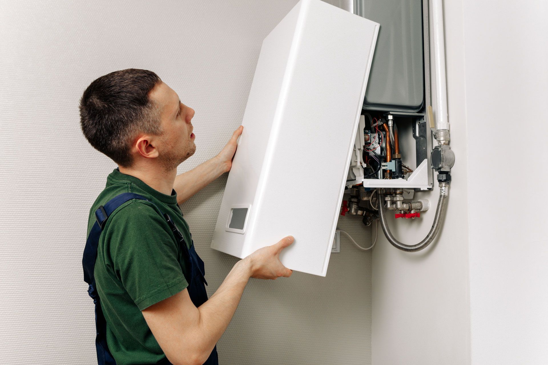 Man installing a white gas boiler on a wall. He is wearing a green shirt and holding the boiler.