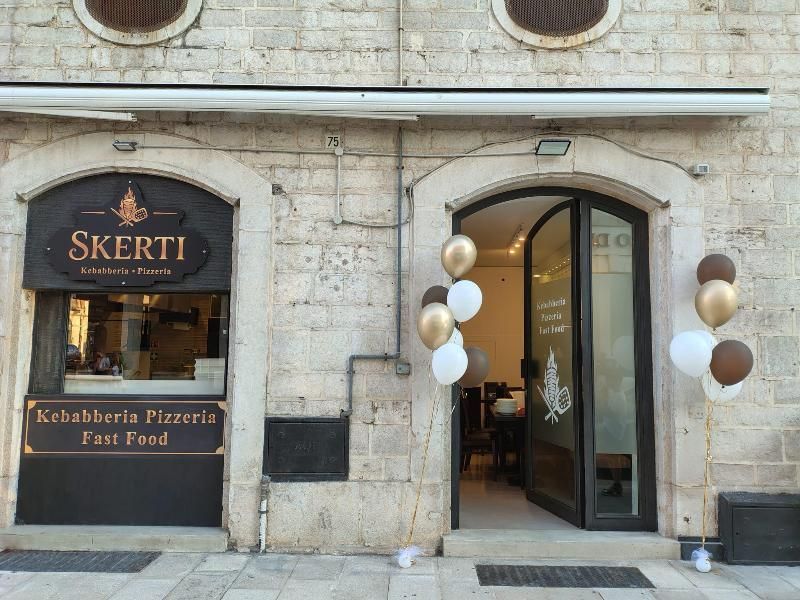 Facciata in pietra del ristorante fast food Skerti, specializzato in kebab e pizza, con palloncini dorati e bianchi all'ingresso.