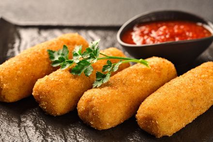 Bastoncini di mozzarella impanati e fritti, guarniti con prezzemolo e serviti con salsa rossa su un piatto scuro.