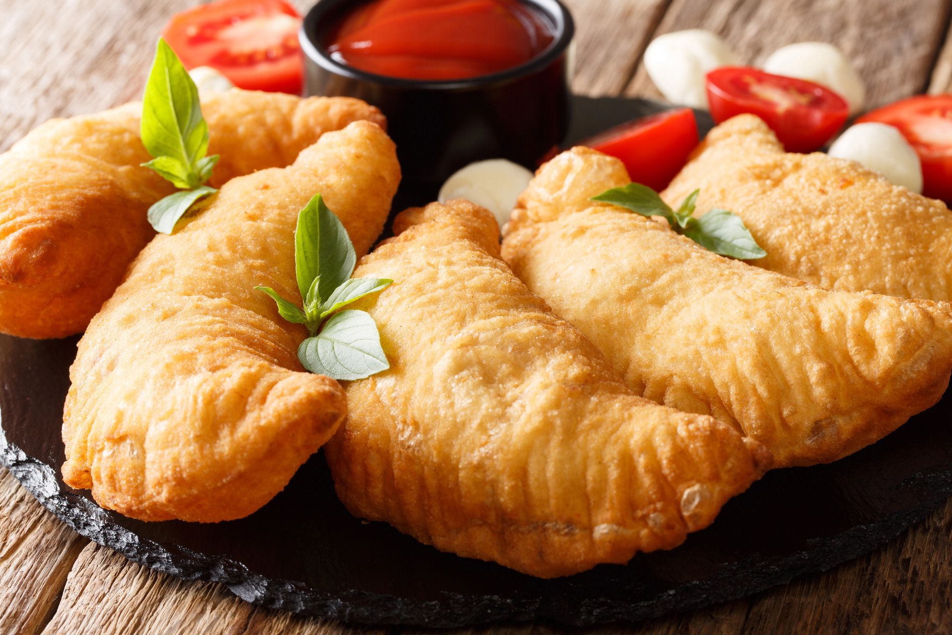 Frittelle dorate guarnite con basilico su un piatto nero con salsa d'accompagnamento e pomodorini ciliegino.