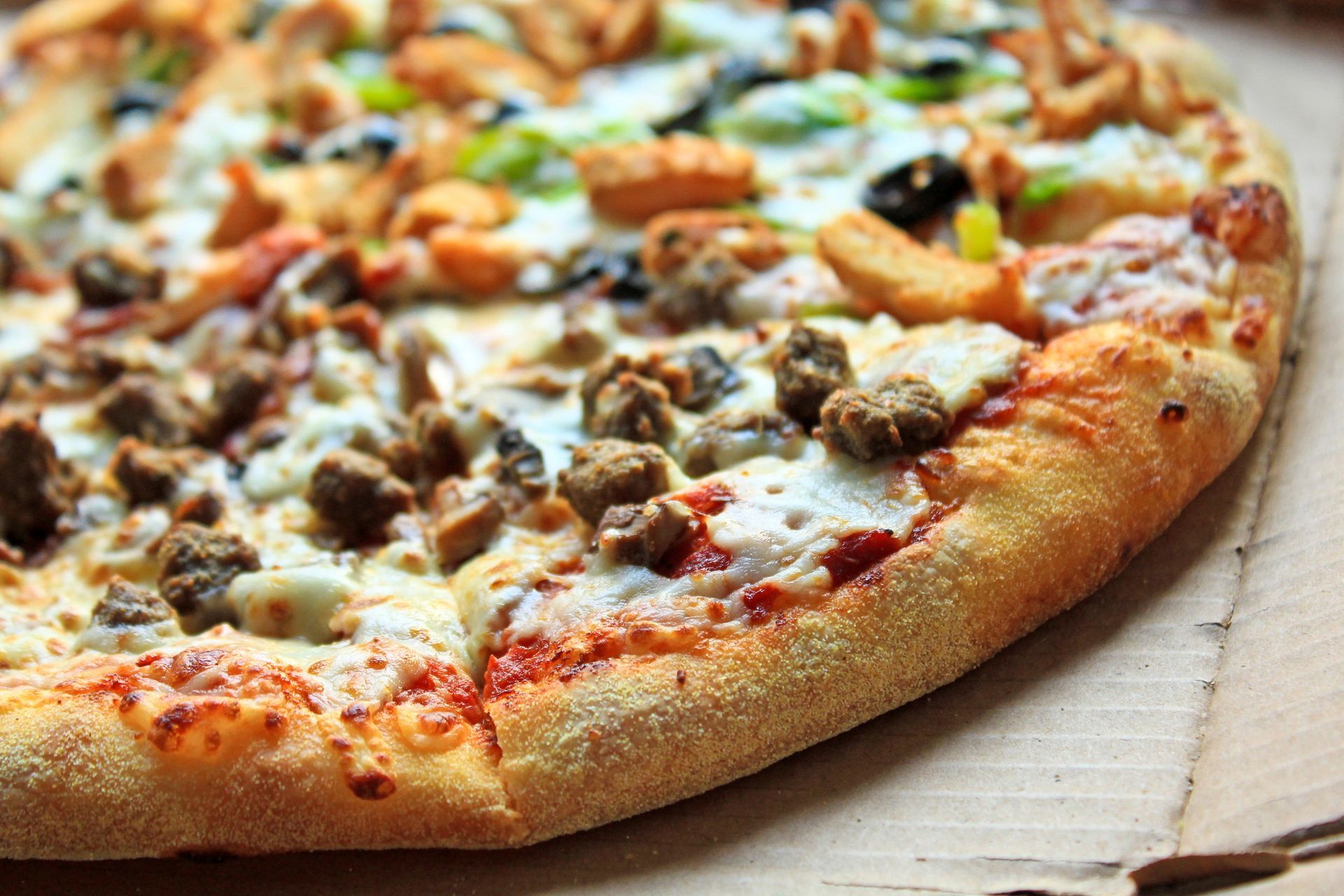 Primo piano di una pizza con peperoni e salsiccia su una scatola di cartone.