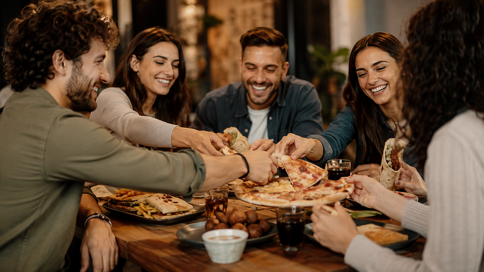 Amici che condividono la pizza e ridono attorno a un tavolo da pranzo in un ambiente caldo e accogliente.