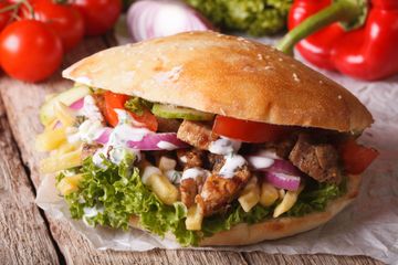 Primo piano di un panino farcito con lattuga, pomodori, cipolle e carne grigliata su legno rustico.