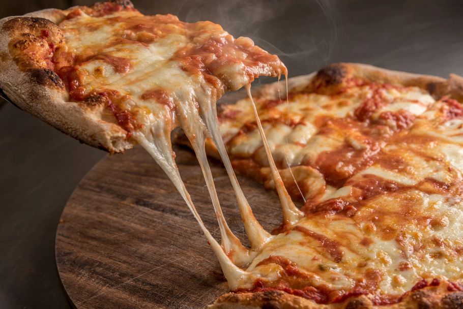 Primo piano di una fetta di pizza ripiena di formaggio che viene sollevata, con il formaggio fuso che si estende su un tagliere di legno.